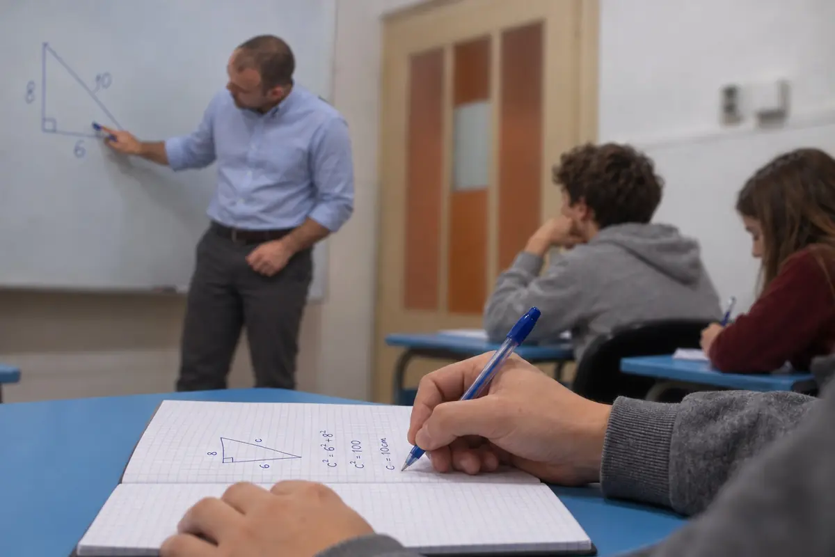 Učenik rešava geometrijski zadatak u svesci, dok se u pozadini radi pred tablom.